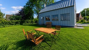 Een modern huis met een groot gazon, een eettafel met stoelen en een kleine tuin.