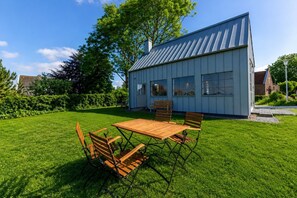 Ein modernes Haus mit großem Rasen, einem Esstisch mit Stühlen und einem kleinen Garten.