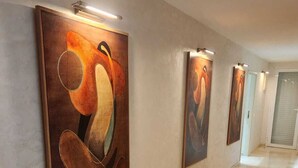 Ein Flur mit drei großen abstrakten Gemälden an der Wand, jeweils eine Leuchte darüber, und einem Schachbrettfußboden.