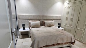 Ein Schlafzimmer mit einem großen Bett, zwei Nachttischen mit Lampen, einem Kleiderschrank und einem gefliesten Boden.