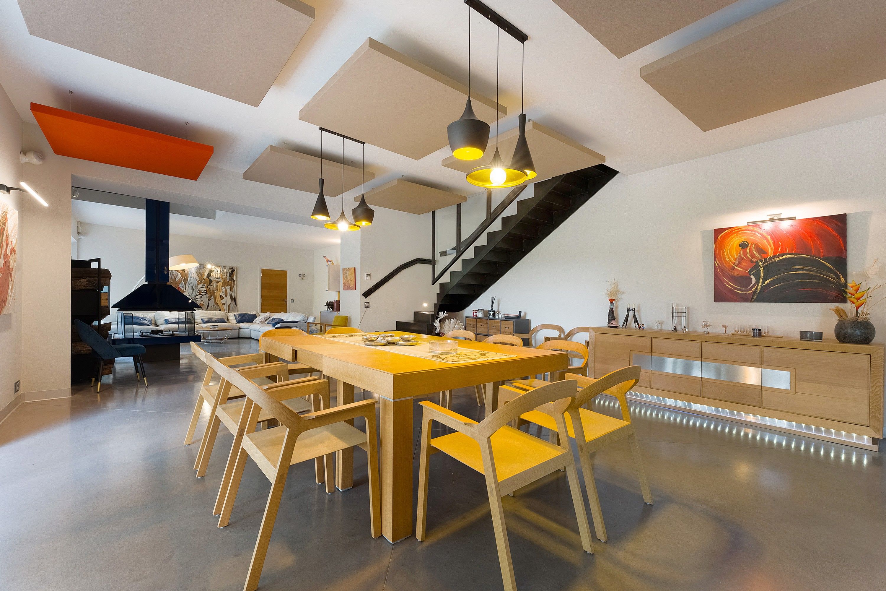 Un vaste espace dédié à la salle à manger, avec une longue table et des chaises en bois, un escalier et une cuisine moderne dotée de meubles en bois.