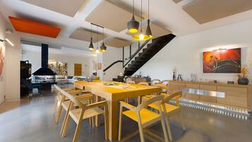 Un vaste espace dédié à la salle à manger, avec une longue table et des chaises en bois, un escalier et une cuisine moderne dotée de meubles en bois.