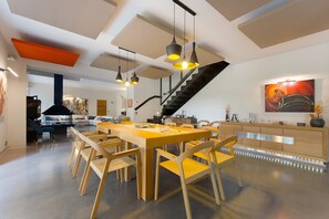 A spacious dining area with a long wooden table and chairs, a staircase, and a modern kitchen with a wooden cabinet.