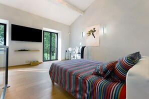 A modern bedroom with a large bed, a flat-screen TV, and a balcony with a view of greenery. - Holiday Home "Bastide Neuve en Provence" with Private Pool, Terrace & Wi-Fi (Caumont-sur-Durance)