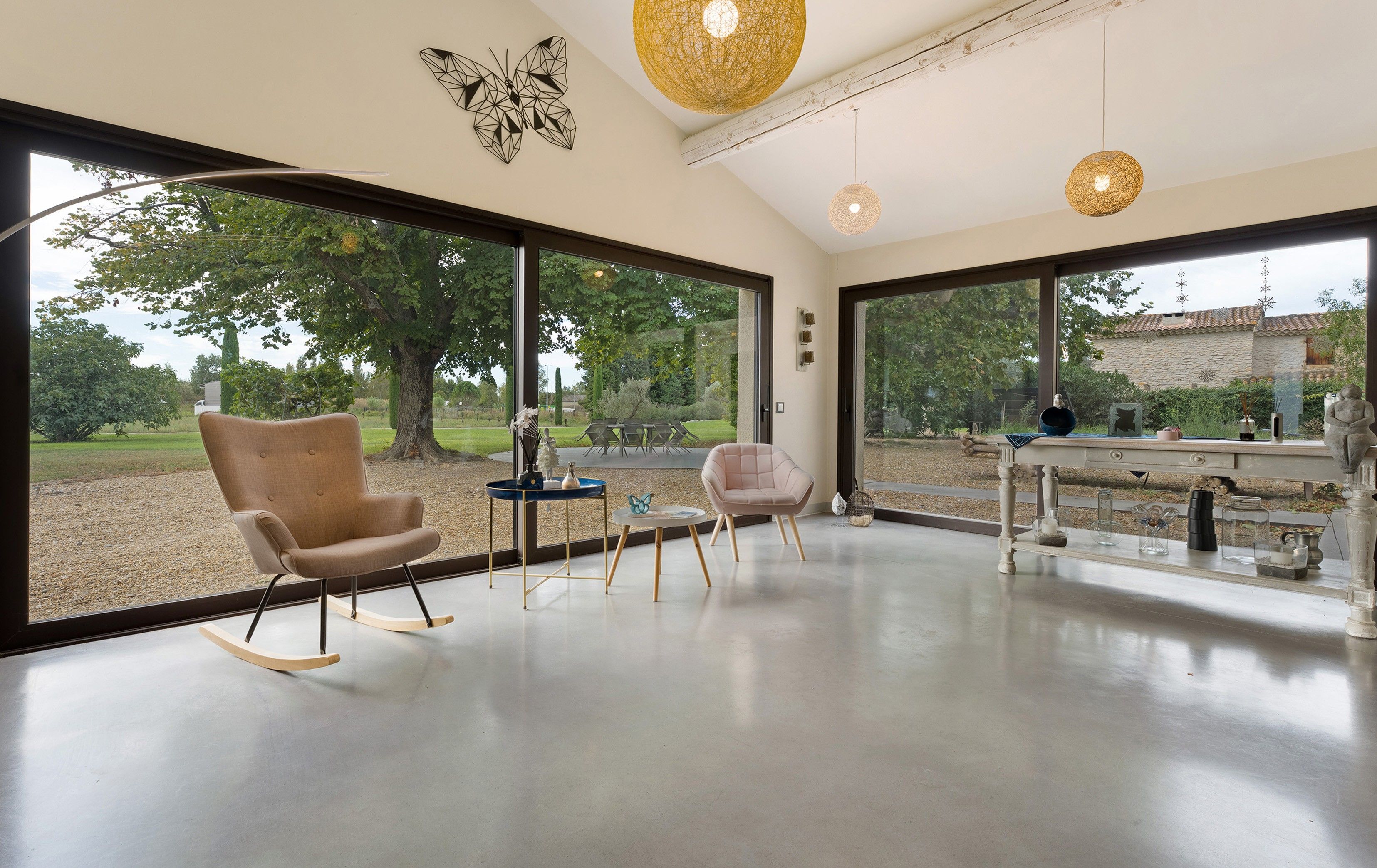A modern interior with large windows, a rocking chair, a small table, and decorative items.