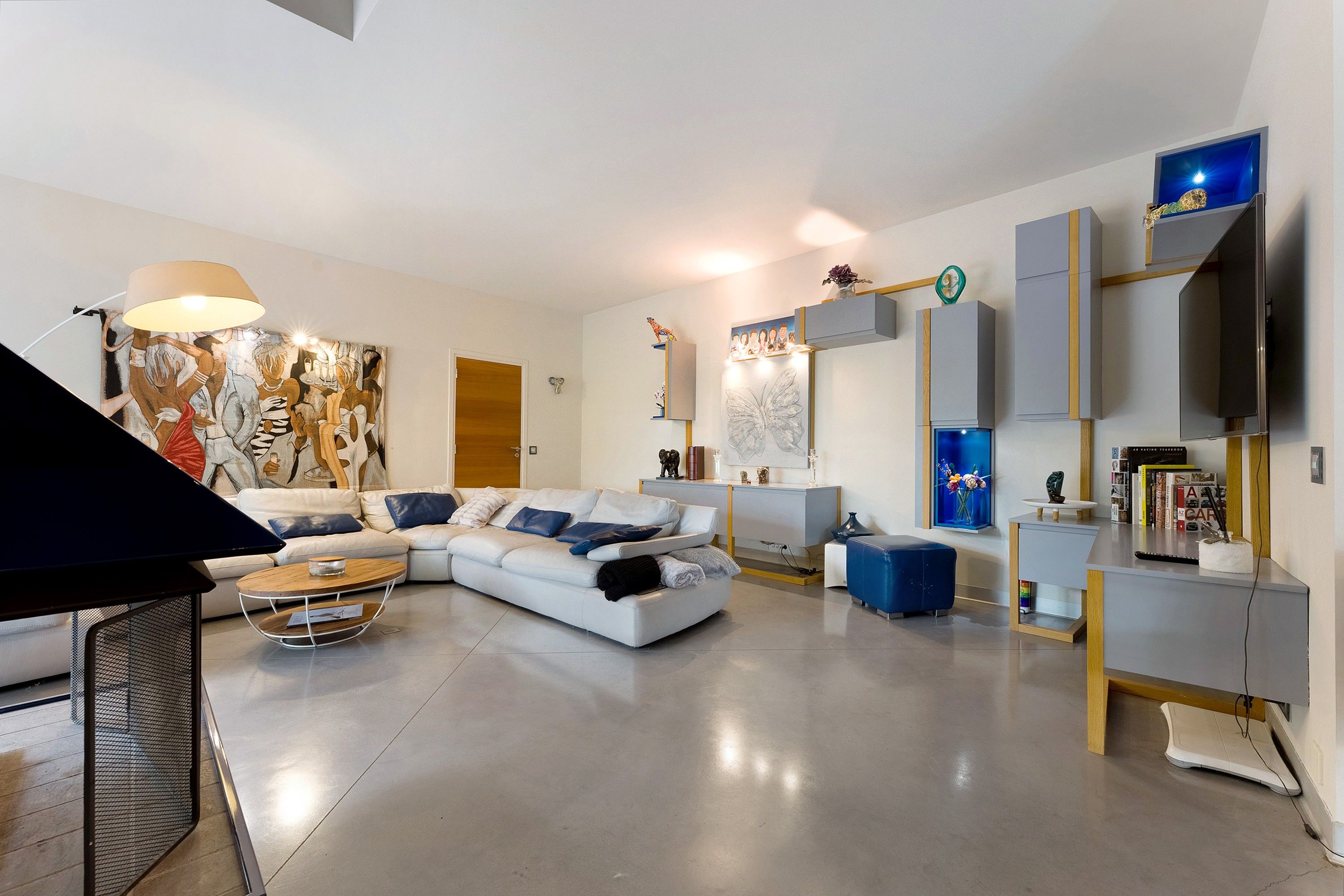A modern living room with a sectional sofa, a coffee table, and a flat-screen TV mounted on the wall.