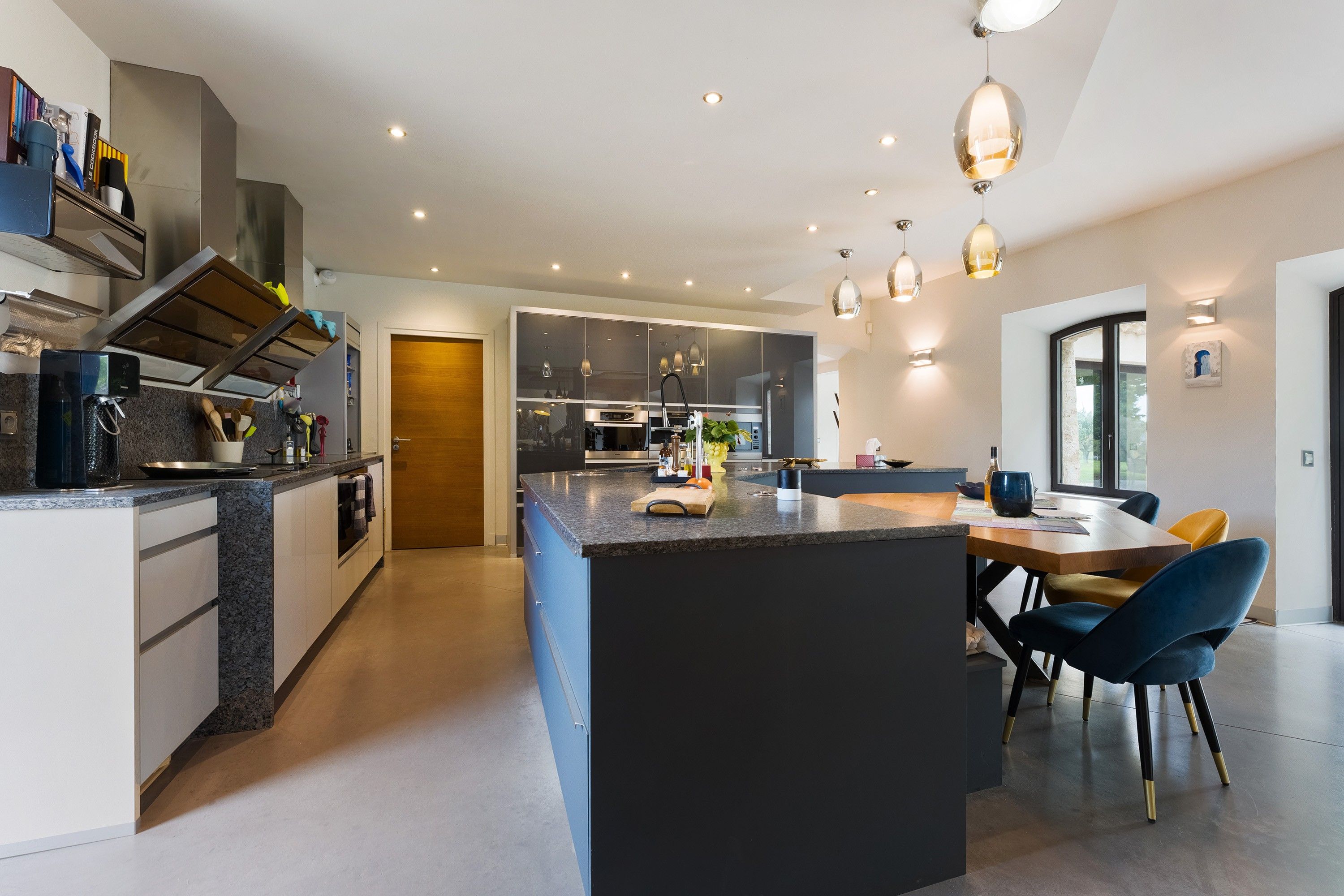 A modern kitchen with a central island, built-in appliances, and pendant lighting.
