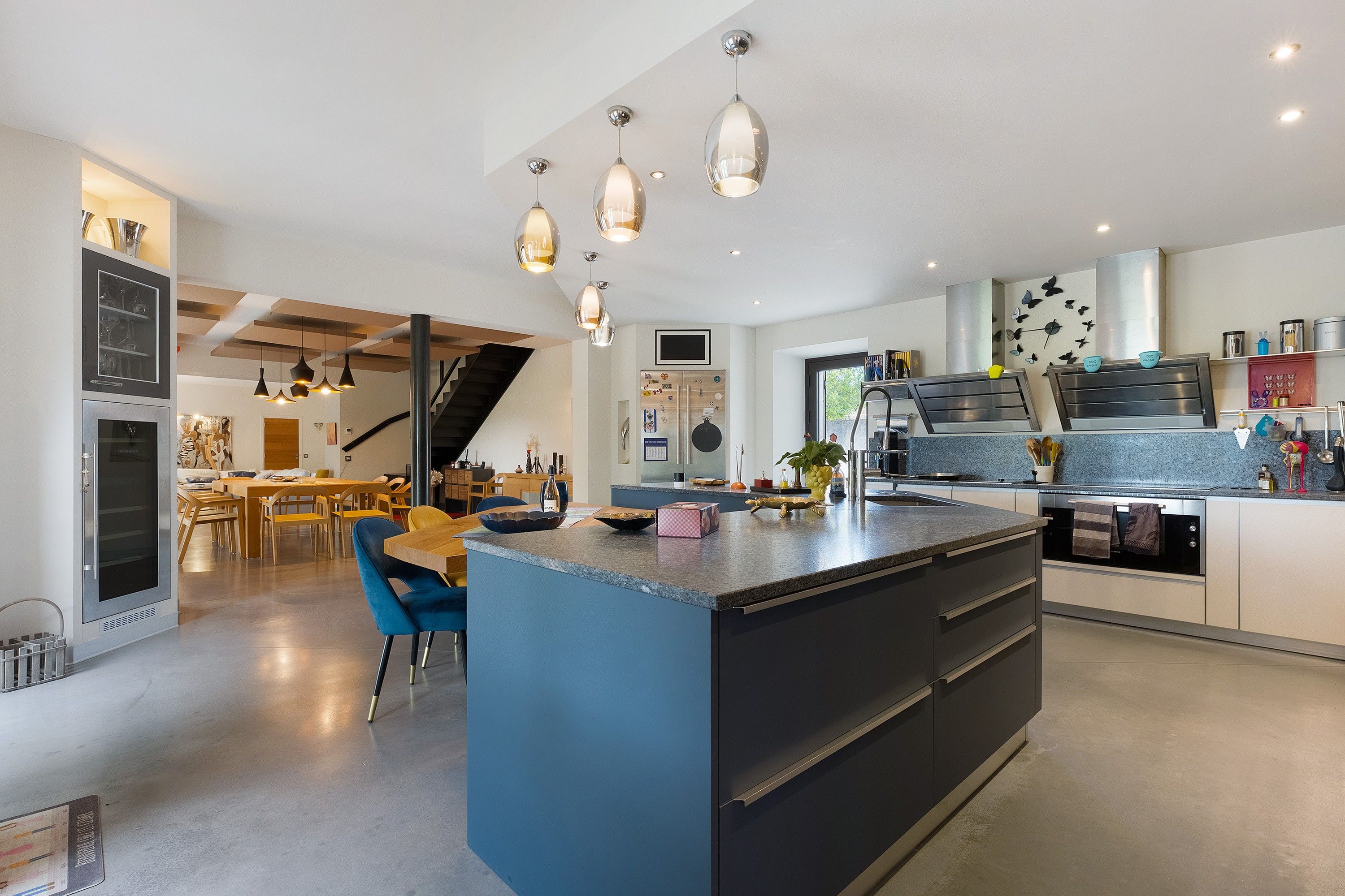 Une cuisine moderne dotée d’un îlot central, de luminaires suspendus et donnant sur l’espace repas.