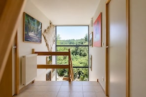A hallway with a view of a forest, a radiator, and artwork on the walls.