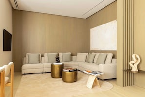 Ein modernes Wohnzimmer mit einem Ecksofa, zwei goldenen Beistelltischen, einer Zeitschrift auf einem Ständer und einer minimalistischen Skulptur.