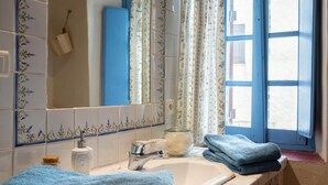 Baño con lavamanos, espejo y ventana con contraventanas azules.