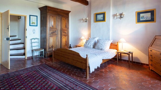 Un dormitorio con cama de madera, mesita de noche, cómoda, silla, alfombra y una escalera que lleva a otra habitación.