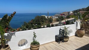 Un balcon agrémenté de plantes en pot, d’une chaise et offrant une vue sur la mer et la ville.