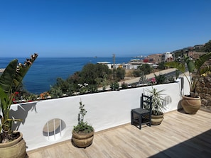 A balcony with potted plants, a chair, and a view of the sea and town. - Algerie Rare, Saket Béjaia T3 exceptional view, face, sea (Bejaia Saket)