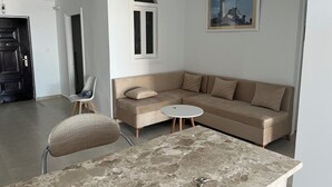 Un salon moderne avec un canapé beige, une petite table ronde, un fauteuil et un tableau accroché au mur.