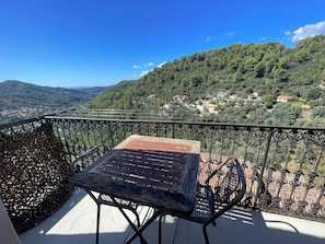 A balcony with a table and chairs, overlooking a mountainous landscape with scattered houses. - Charming house in the heart of the medieval village of Peillon - between Nice and Monaco. (Peillon)