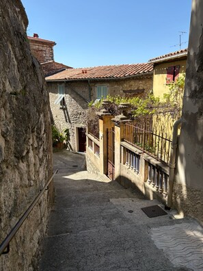 A narrow stone pathway leading to a building with a tiled roof and a stone wall on one side. - Charming house in the heart of the medieval village of Peillon - between Nice and Monaco. (Peillon)