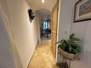 A hallway with a stone floor, a wooden door, a wall-mounted decorative item, and a potted plant. - Charming house in the heart of the medieval village of Peillon - between Nice and Monaco. (Peillon)