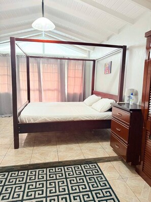 A four-poster bed with a wooden frame, a bedside table with drawers, a patterned rug, and a ceiling fan.