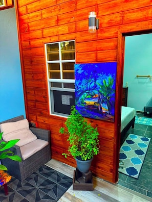 Interior de una cabaña de madera con una ventana, un cuadro, una planta en maceta, un sofá y una cama.