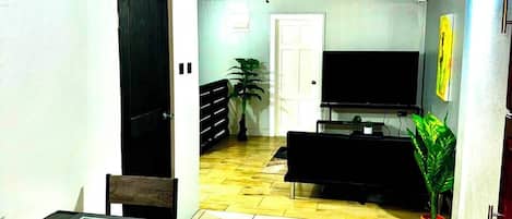 Un coin repas avec une table et des chaises, un ventilateur de plafond, un téléviseur et une plante, le tout situé dans un salon dont le sol est carrelé.