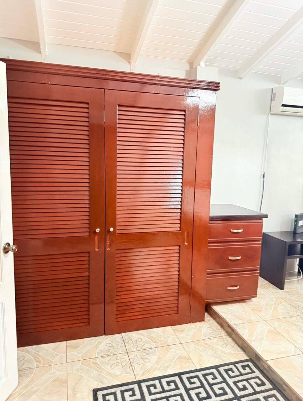 Una habitación con un armario de madera grande, un escritorio pequeño y una alfombra estampada.