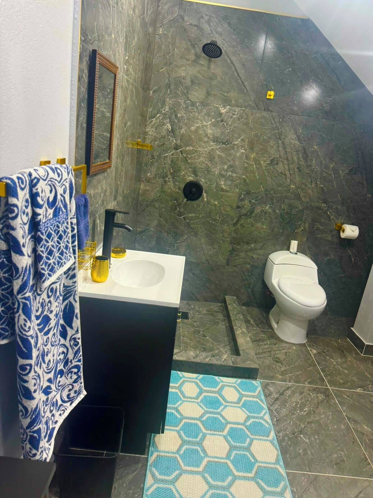 A bathroom with a marble wall, a sink, a toilet, and a patterned rug.