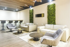 Ein moderner Loungebereich mit einer Couch, Sesseln, einem Couchtisch und einer Rezeption.
