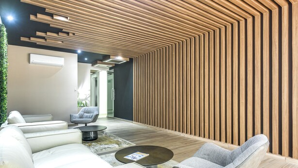 Un interior moderno con un muro de listones de madera, un sofá blanco, un sillón gris y una pequeña mesa redonda.