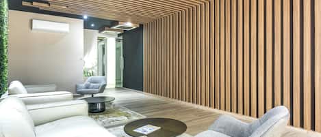 Un interior moderno con un muro de listones de madera, un sofá blanco, un sillón gris y una pequeña mesa redonda.