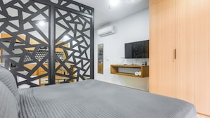 Un dormitorio con cama, televisión, armario y separador con diseño geométrico.