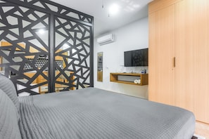 A bedroom with a bed, a TV, a wardrobe, and a partition with a geometric pattern. - Walk to Beach & 5th Ave! Chic Studio w/ Patio (Playa del Carmen)
