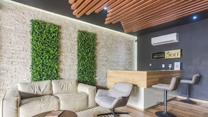 Un área de descanso moderna con pared de ladrillo, jardines verticales verdes, un sofá de cuero, una mesa de centro redonda y un mostrador de recepción de madera.
