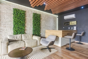 A modern lounge area with a brick wall, green vertical gardens, a leather sofa, a round coffee table, and a wooden reception desk. - Walk to Beach & 5th Ave! Chic Studio w/ Patio (Playa del Carmen)