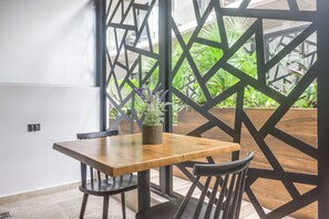 Ein Essbereich mit einem Holztisch und Stühlen, einer Topfpflanze und einem geometrischen Wandmuster.