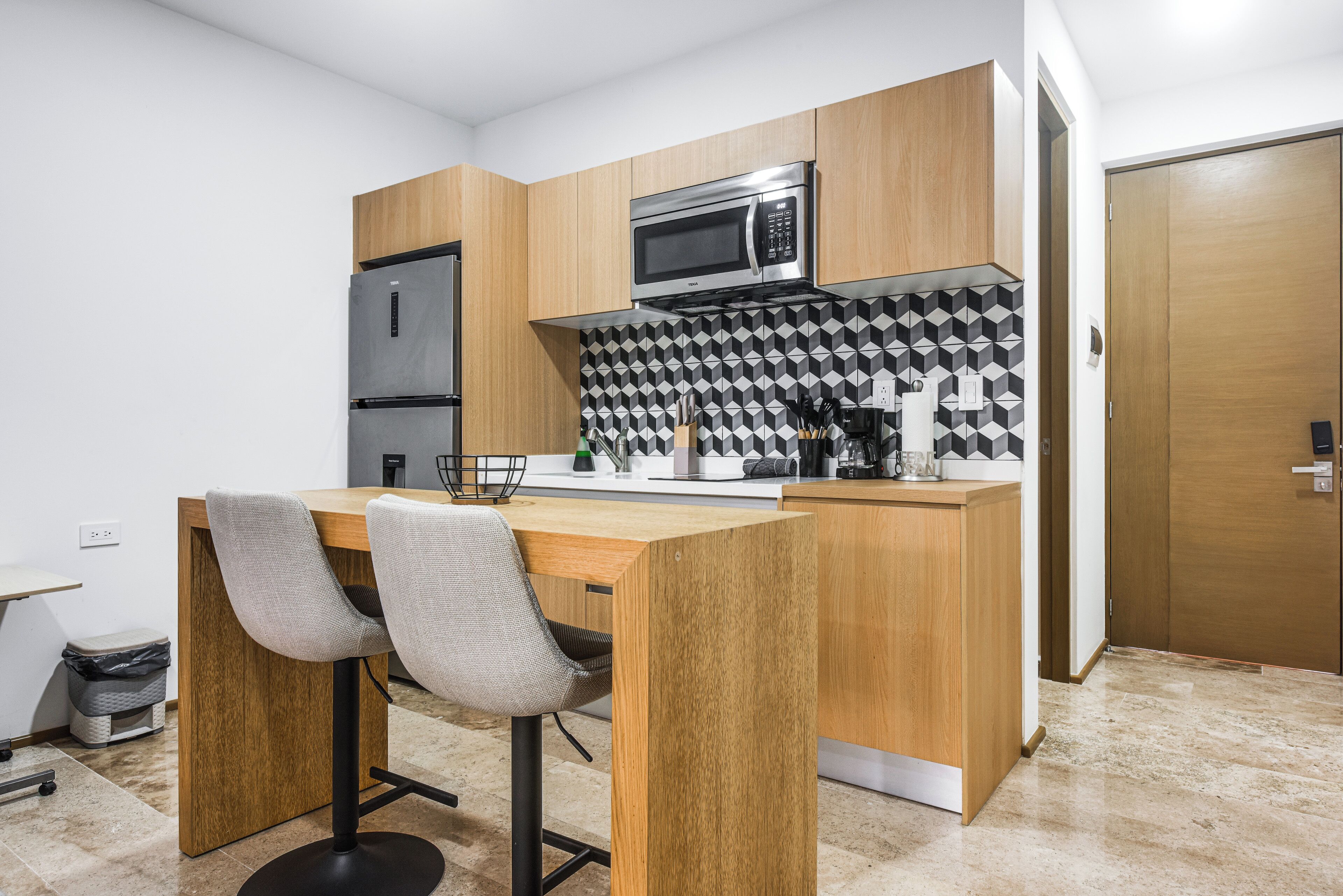 Une cuisine moderne dotée de meubles en bois, d’un réfrigérateur en acier inoxydable, d’un four à micro-ondes et d’un coin repas avec une table en bois et deux chaises.