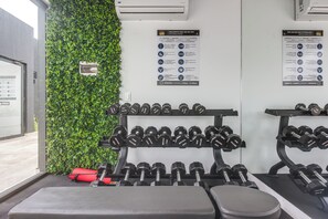 Ein Fitnessraum mit an der Wand befestigten Kurzhanteln, einer Bank und einer grünen Wand.