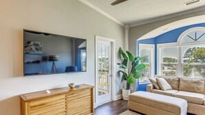 A living room with a wooden cabinet, a beige sofa, a large potted plant, and a flat-screen TV mounted on the wall.