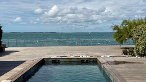 Um deck de madeira com piscina, com vista para um corpo d'água e uma costa distante.