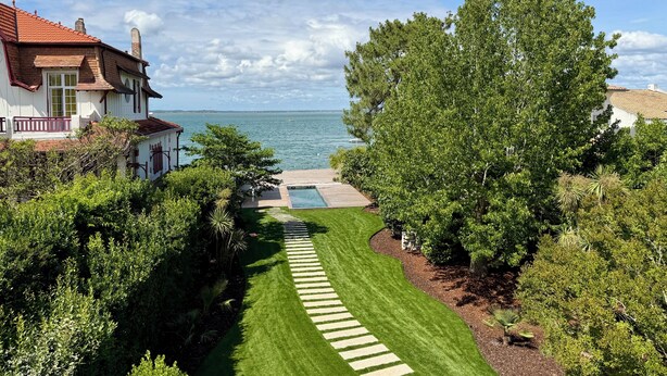 Um jardim bem cuidado com um caminho definido que leva a uma piscina, cercada por vegetação exuberante e vista para o mar.
