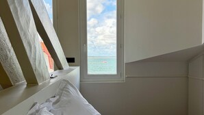 Um quarto com cama, janela e vista para o mar, além de teto inclinado.