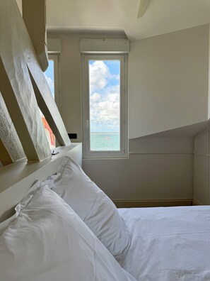 Ein Schlafzimmer mit Bett, einem Fenster mit Meerblick und einer schrägen Decke.