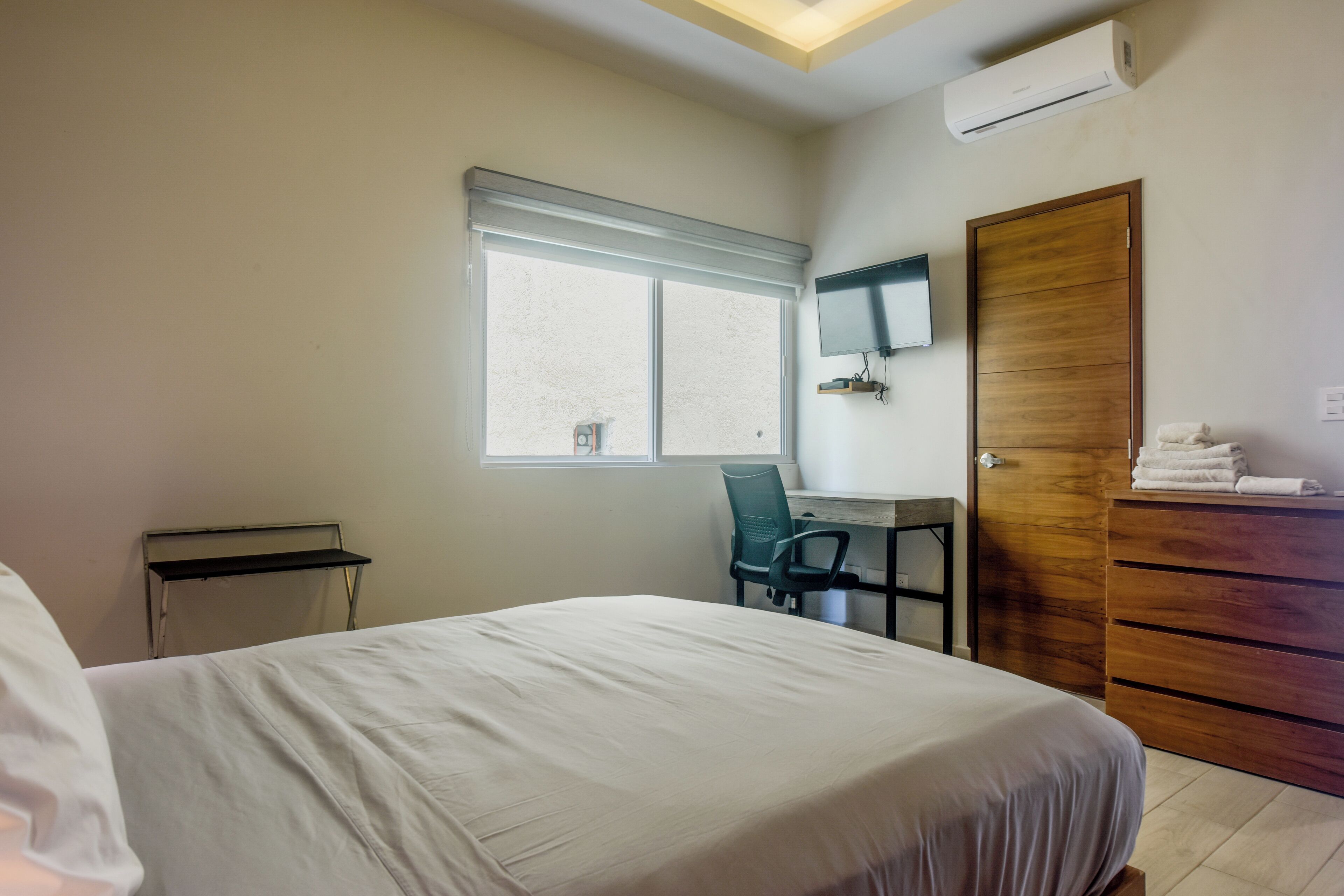 A bedroom with a bed, a desk, a chair, a TV, and a wardrobe.