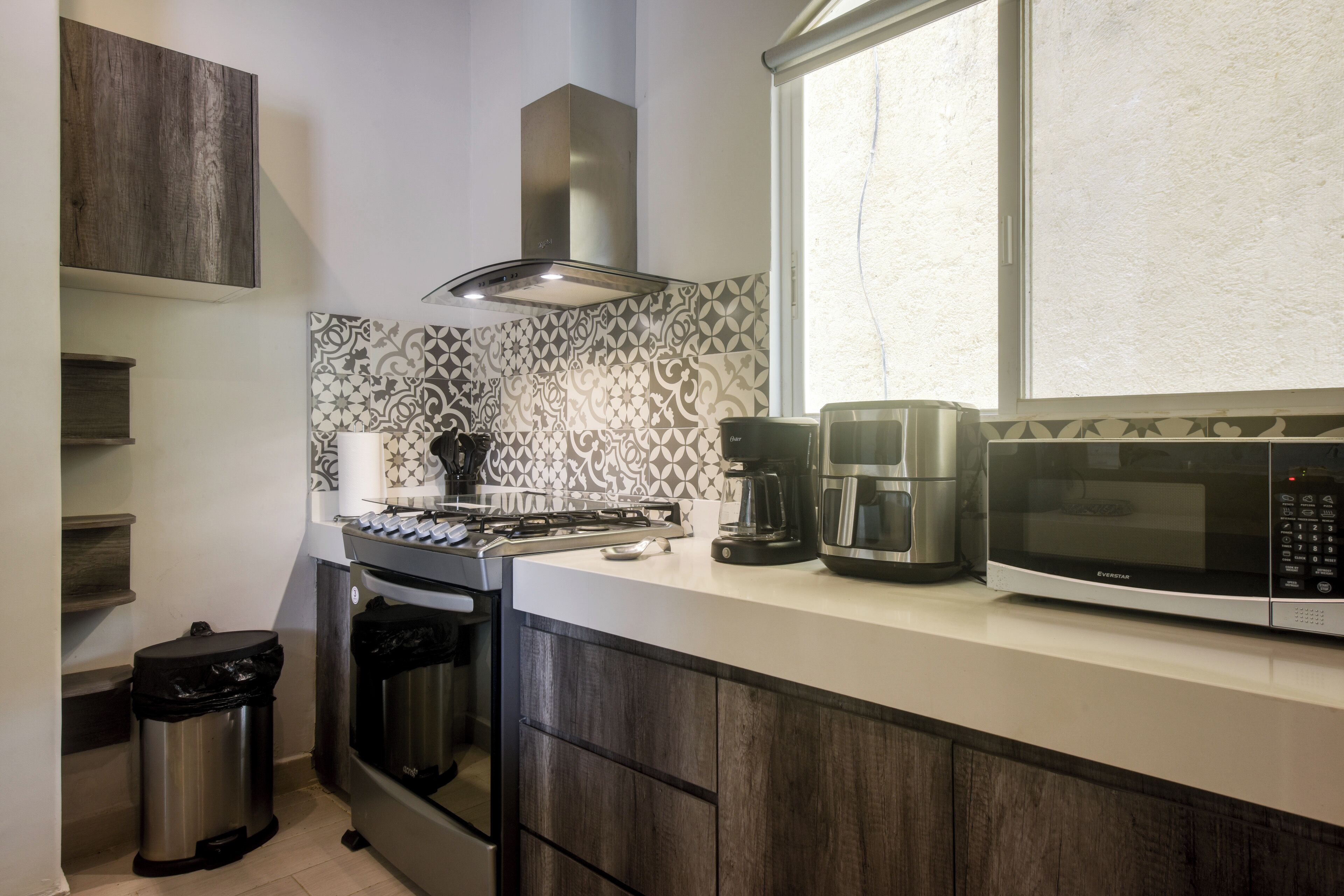 A kitchen with a gas stove, coffee maker, microwave, and a window with a view.