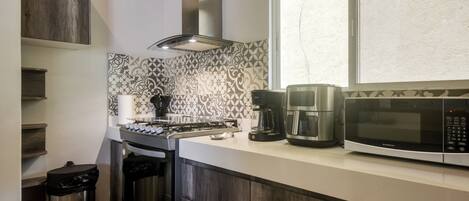 A kitchen with a gas stove, coffee maker, microwave, and a window with a view.