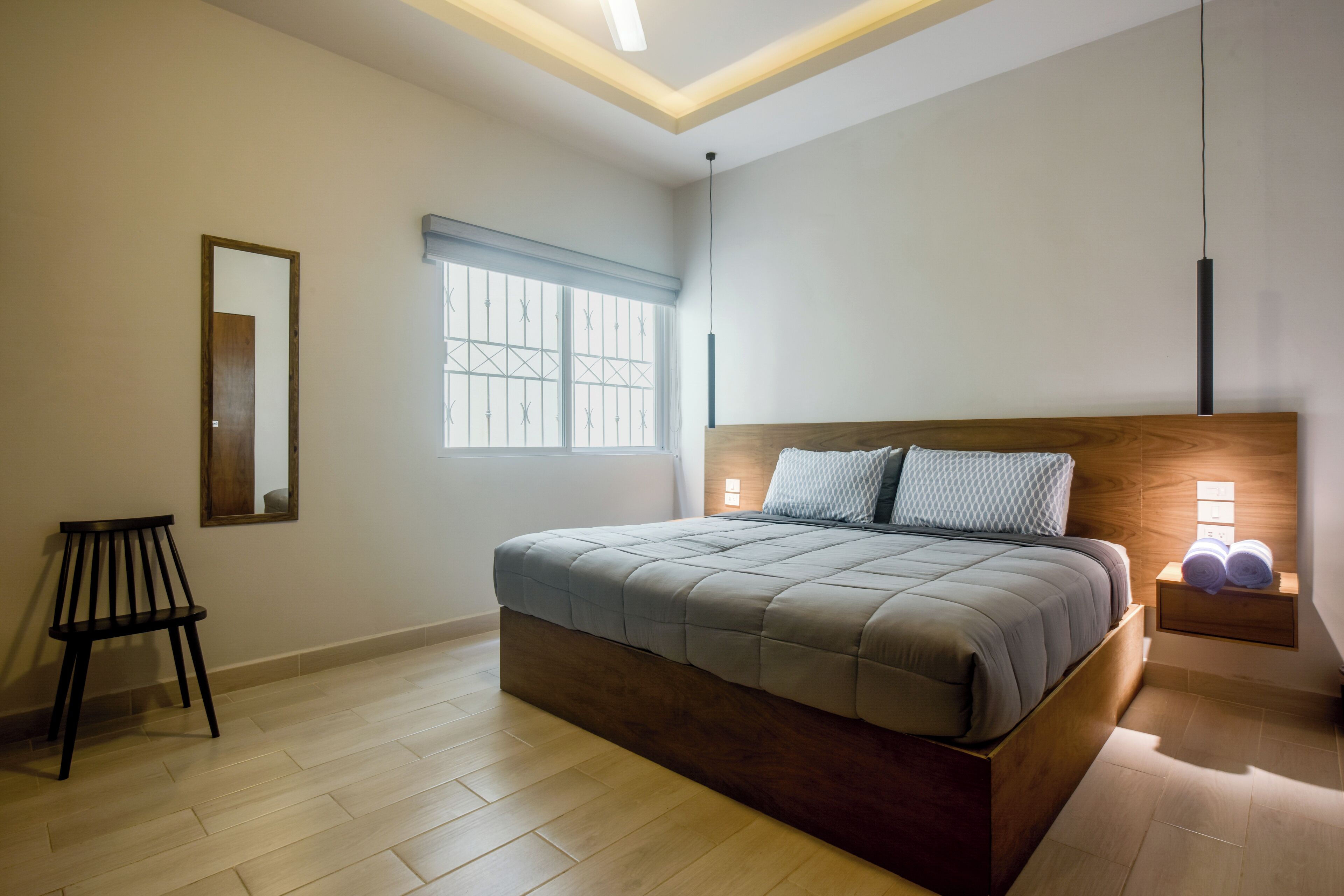 Ein Schlafzimmer mit Bett, Nachttisch, Stuhl, Fenster und Spiegel.
