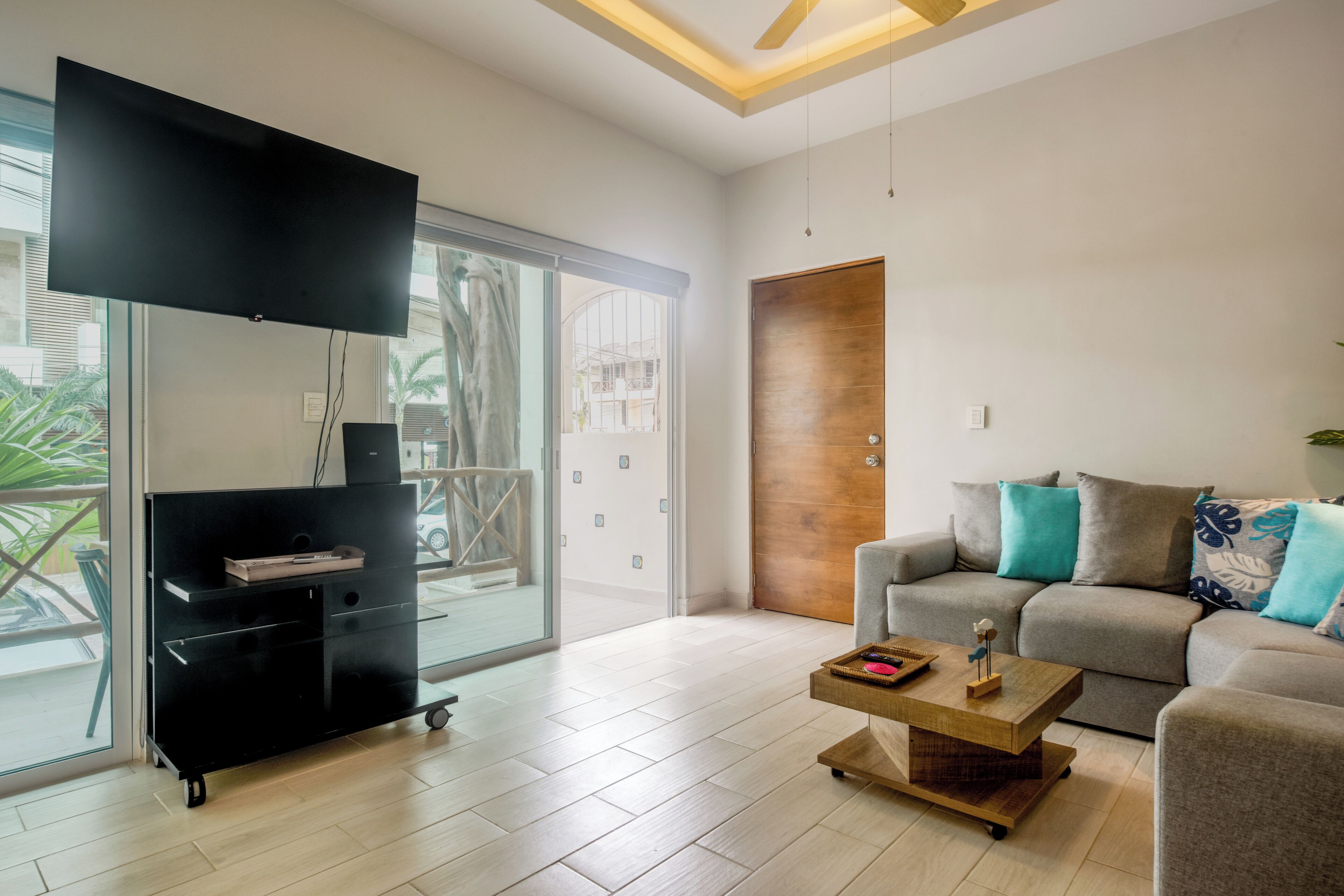 A modern living room with a flat-screen TV, a sofa, a coffee table, and a sliding glass door leading to a balcony.