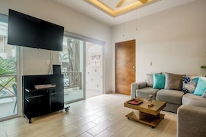 Ein modernes Wohnzimmer mit Flachbildfernseher, einer Couch, einem Couchtisch und einer Glastür zum Balkon.