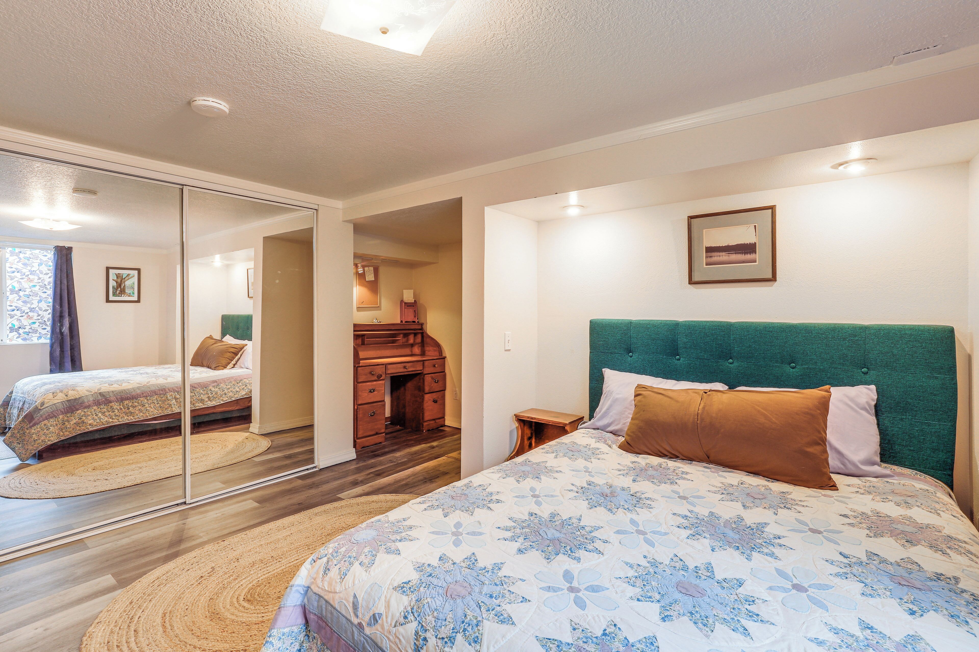 Une chambre à coucher avec un grand lit, une tête de lit verte, un miroir et une commode en bois.