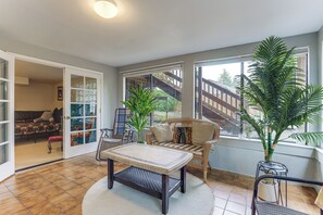 A room with a dining table, wicker furniture, a potted plant, and a view of a building outside. - Unique Unit w/ Patio & Grill in Portland Area! (Milwaukie)